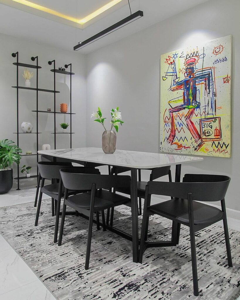 Dining area in gray living room by Mandora Design showing colourful wall art and black steel shelf.