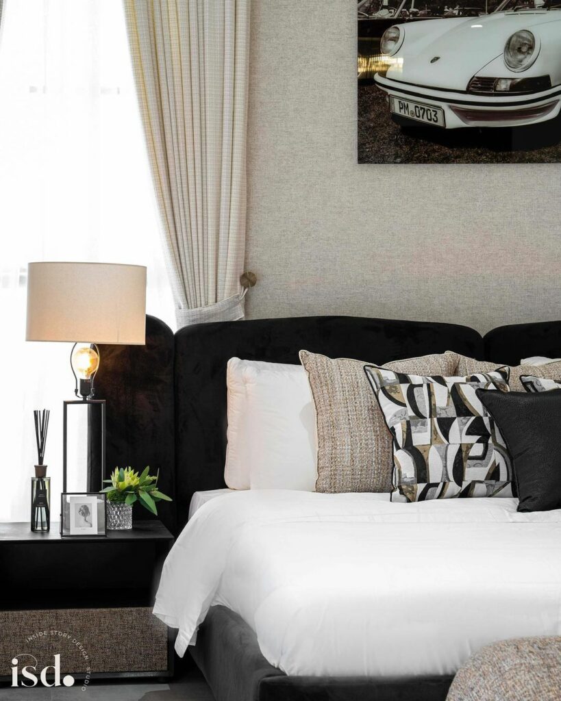 A view of the contemporary bedroom showing the cream drapes, black upholstered bed, table lamp and other accessories on the nightstand.