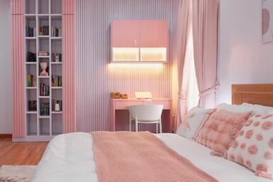 Girl's bedroom decorated in pastel pink, showcasing a bed, study area, and bookshelf from a side angle.