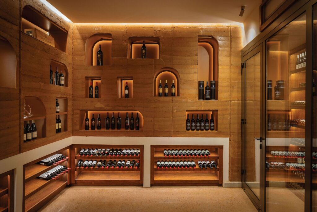 A luxurious wine cellar with neatly organized wine bottles on wooden shelves and racks, surrounded by warm ambient lighting, featuring a sand-colored stone interior.