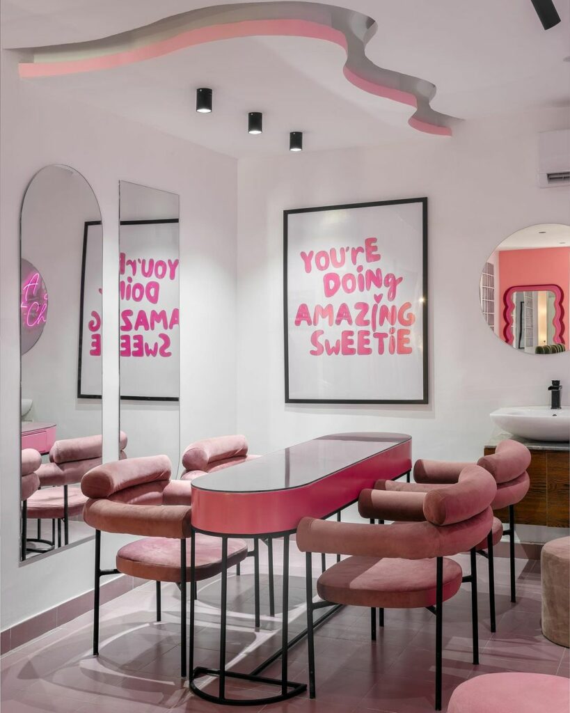 A pink salon with matching pink chairs and a table with black steel frame, with a wavy ceiling design creating a chic and feminine atmosphere.