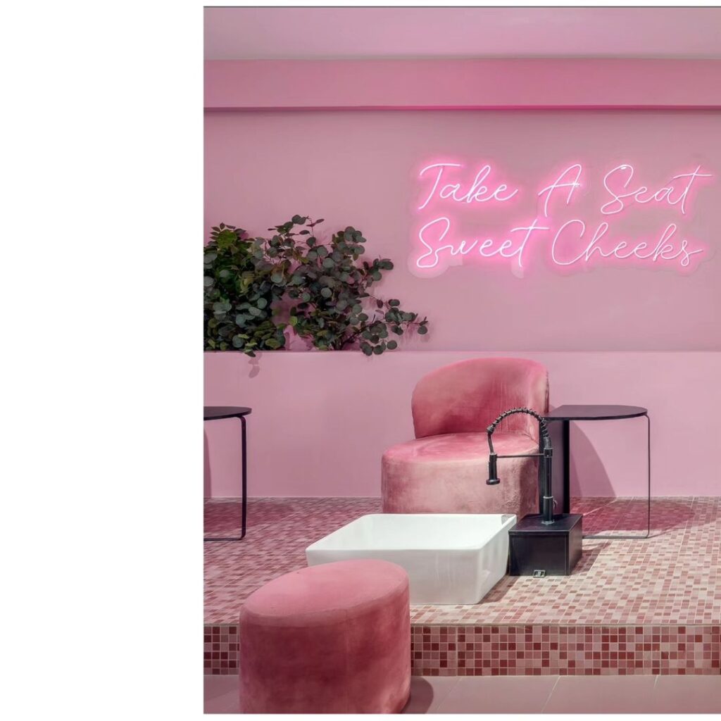 A pink salon with a pedicure station with a neon sign and planting behind.