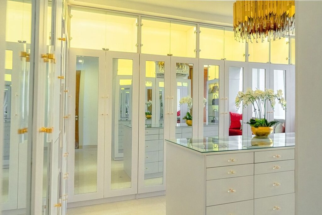 A luxurious walk-in closet with mirrored doors and a sparkling chandelier with a glass-top island.