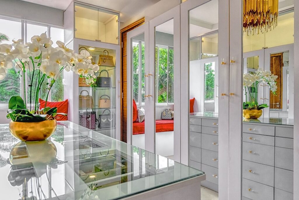 A luxurious walk-in closet with mirrored doors and a sparkling chandelier with a glass top island.