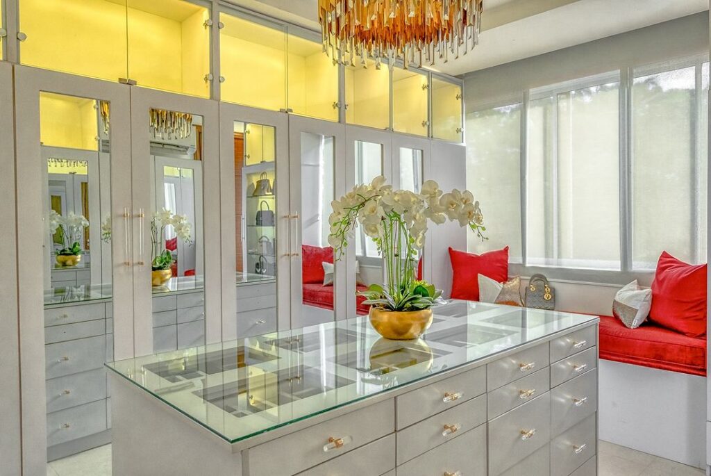 A luxurious walk-in closet with mirrored doors and a sparkling chandelier with a glass top island.