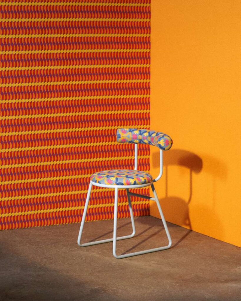 A chair placed against a vibrant orange wall adorned with a lively and colorful pattern.