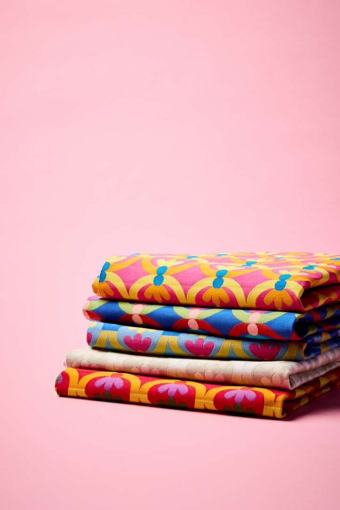 A vibrant stack of fabric on a pink background, showcasing a variety of colors and textures.