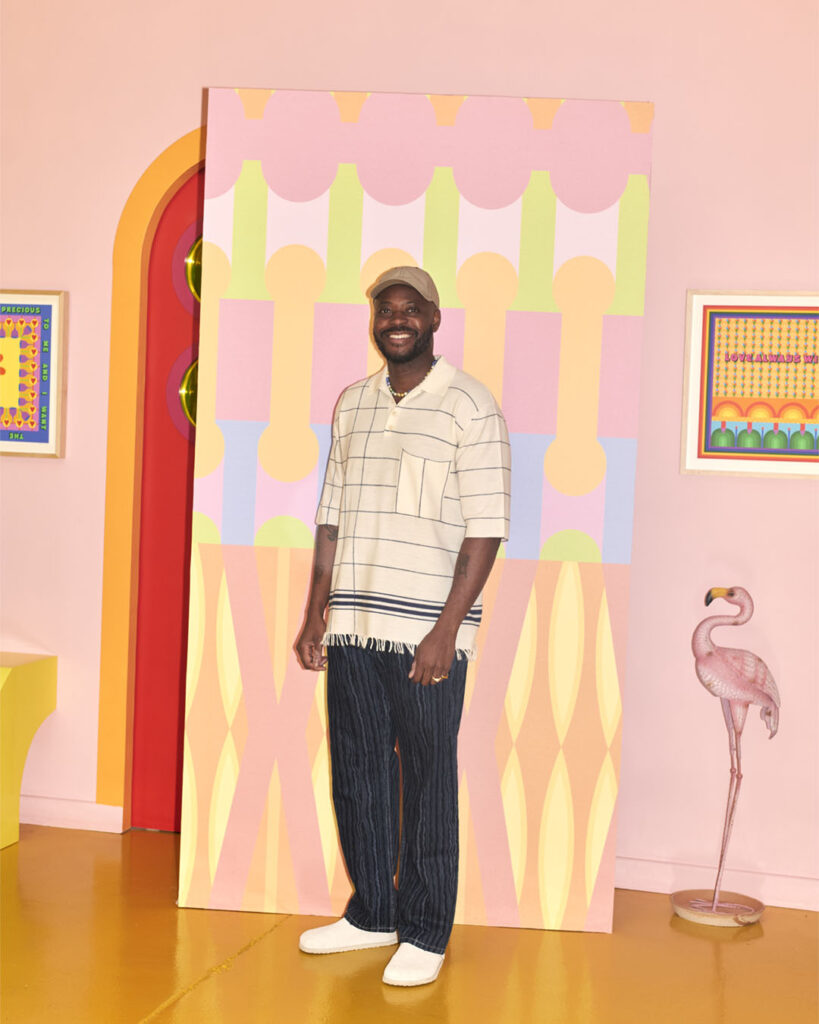 A man posing in front of a pink wall.