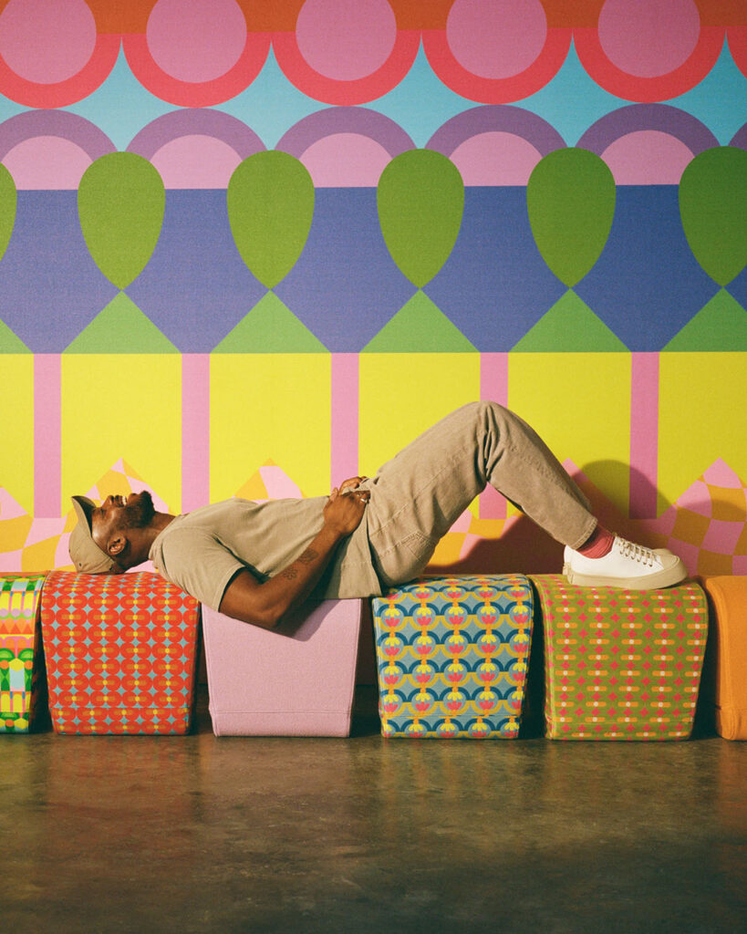 A man lying on colorful seats in front of a vibrant wall, enjoying a sunny day in the park.