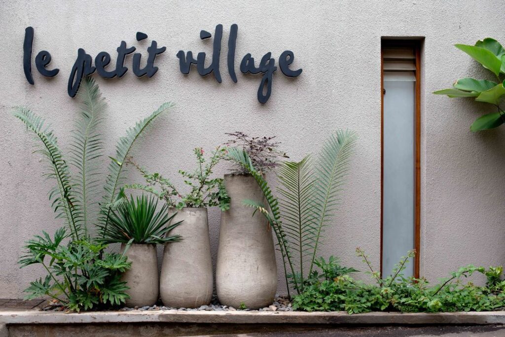 Sign reading "Le Petit Village" in front of charming French-style building.
