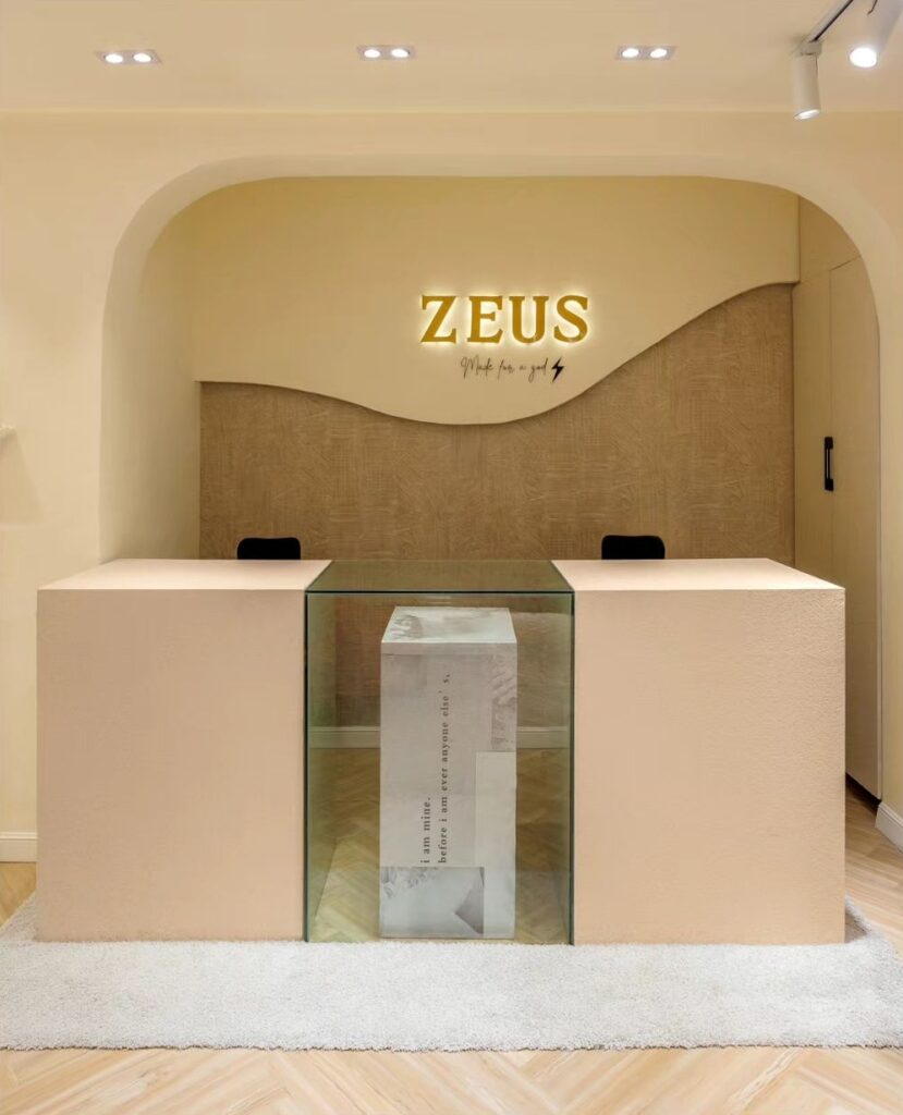 Reception area with glass reception desk with the word "Zeus" on the wall behind.