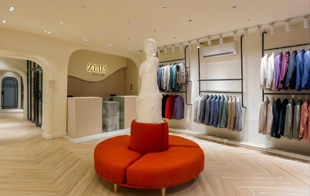 Reception area in store with metal hangers for clothing display and a round seating area for visitors.