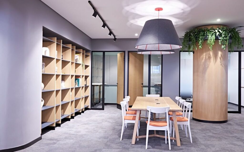 Collaborative space in office with indoor planting incorporated displaying and extensive use of wood in the doors, shelving and walls.