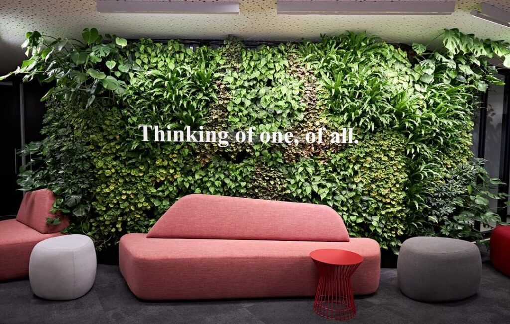 A waiting area with distinctive seating and a green wall with signage saying: Thinking of one, of all.