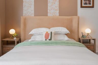 Bedroom setting featuring white bed, pillows, and wooden nightstand with rattan front.