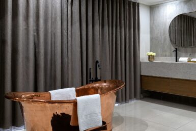 A bathroom with a glass shower and a freestanding soaking copper bathtub.