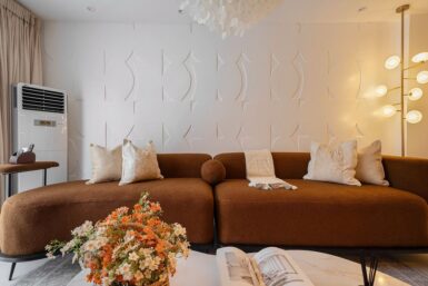 Brown curved sectional sofa with textured wall behind it.